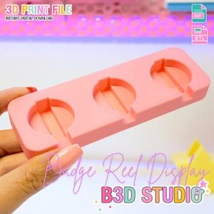 May include: A pink 3D-printed badge reel display with three circular slots. The text "3D PRINT FILE" and "INSTANT DIGITAL DOWNLOAD" are visible at the top. The words "Badge Reel Display" and "B3D STUDIO" are also present.