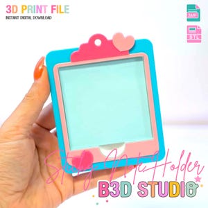 以下が含まれることがあります： 青とピンクの3Dプリントアートホルダー。ハート型のアクセント付き。ホルダーは長方形のフレームで、内側は水色です。画像には「3D PRINT FILE」と「B3D STUDIO」と書かれています。