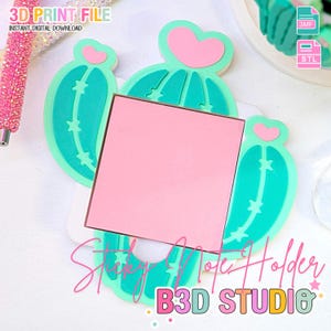 Puede incluir: Un soporte para notas adhesivas en forma de cactus turquesa y rosa con un bloc de notas cuadrado rosa. El soporte tiene una parte superior en forma de corazón y detalles de estrellas. El texto en la imagen dice "3D PRINT FILE" y "Sticky Note Holder B3D STUDIO".