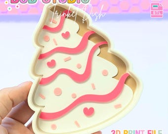May include: A cream-colored Christmas tree-shaped cookie cutter with pink icing details, including hearts and sprinkles. The cutter has a light brown interior and is held by a hand. Text on the image reads "B3D STUDIO" and "Trinket Dish".