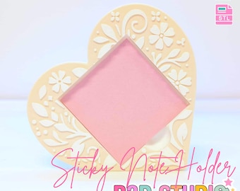 Peut inclure: Un porte-bloc-notes en forme de cœur de couleur crème, orné de motifs floraux et de feuilles. Il comporte un carré rose au centre pour les notes. Le texte sur l'image indique "3D PRINT FILE" et "Sticky Note Holder".