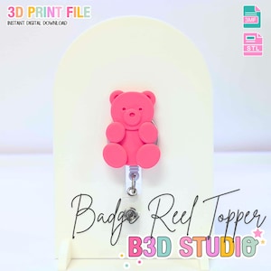 May include: A pink teddy bear badge reel topper. The topper is attached to a white retractable reel. The image also includes the text "Badge Reel Topper" and "B3D STUDIO". The words "3D PRINT FILE" and "INSTANT DIGITAL DOWNLOAD" are also visible.