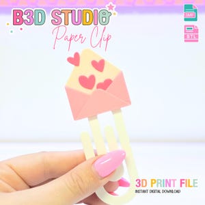 May include: A pink and cream-colored paper clip shaped like an envelope with three pink hearts. The paper clip has a cream-colored base and the text "B3D STUDIO Paper Clip" is visible in the background. The words "3D PRINT FILE" and "INSTANT DIGITAL DOWNLOAD" are also visible.