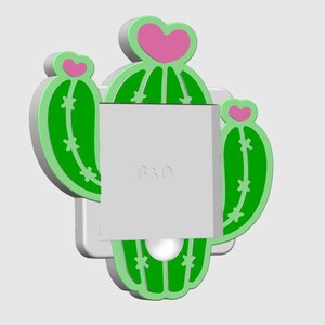 May include: A green and pink cactus-shaped wall decor with a white base. The cactus has a heart-shaped top and star-shaped details. The text "R&D" is visible on the white surface.