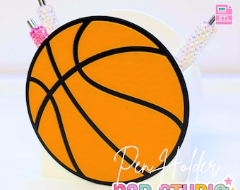 May include: A basketball-themed pen holder with an orange and black design. The pen holder is in the shape of a basketball, with black lines outlining the ball's panels. The text "Pen Holder" and "B3D STUDIO" are visible. The image also includes the text "3D PRINT FILE" and "INSTANT DIGITAL DOWNLOAD".