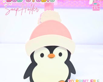 May include: A whimsical soap holder shaped like a penguin wearing a pink hat with a white brim and pom-pom. The penguin has a black body, white belly, and orange feet and beak. The text "B3D STUDIO Soap Holder" and "3D PRINT FILE" are visible.