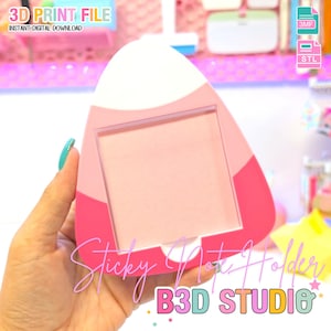 Può includere: Un portablocco rosa e bianco con apertura rettangolare. Il supporto ha una parte superiore arrotondata ed è etichettato "Sticky Note Holder" e "B3D STUDIO". L'immagine include anche il testo "3D PRINT FILE" e icone di tipo di file.