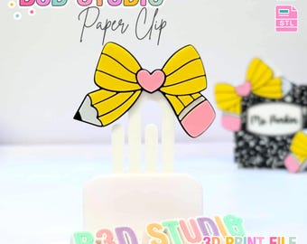 May include: A 3D-printed paper clip shaped like a pencil bow with a pink heart in the center. The text "B3D STUDIO Paper Clip" is displayed above the pencil bow. The base of the paper clip is white, and the text "B3D STUDIO 3D PRINT FILE" is at the bottom.