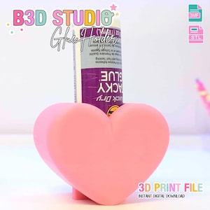May include: A pink heart-shaped glue holder with a tube of glue. The holder has the text "B3D STUDIO Glue Holder" and "3D PRINT FILE INSTANT DIGITAL DOWNLOAD". The glue is purple and white. The holder is designed to hold a glue stick.