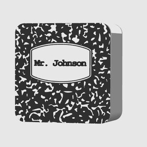 May include: A composition notebook with a black and white speckled pattern. The notebook has a white label with the text "Mr. Johnson" in black. The notebook is rectangular with rounded corners.