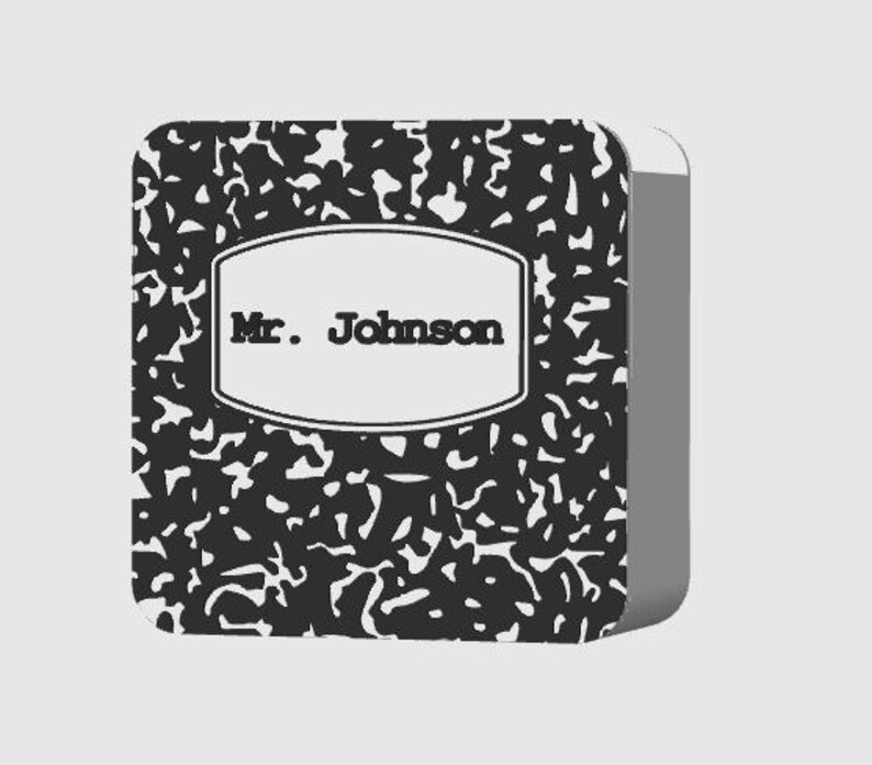 May include: A composition notebook with a black and white speckled pattern. The notebook has a white label with the text "Mr. Johnson" in black. The notebook is rectangular with rounded corners.