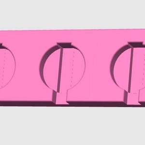 May include: A pink silicone mold for making three round-shaped treats. Each cavity has a vertical divider and a small stem at the bottom. The mold is rectangular with rounded corners and is designed for easy removal of the treats.