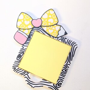 Peut inclure: Un porte-m&eacute;mo d&eacute;coratif avec un n&oelig;ud jaune &agrave; c&oelig;urs blancs, un c&oelig;ur rose et un crayon. Le porte-m&eacute;mo a un carr&eacute; jaune pour les notes, pos&eacute; sur un cadre &agrave; motifs noir et blanc. Un design mignon et fantaisiste.