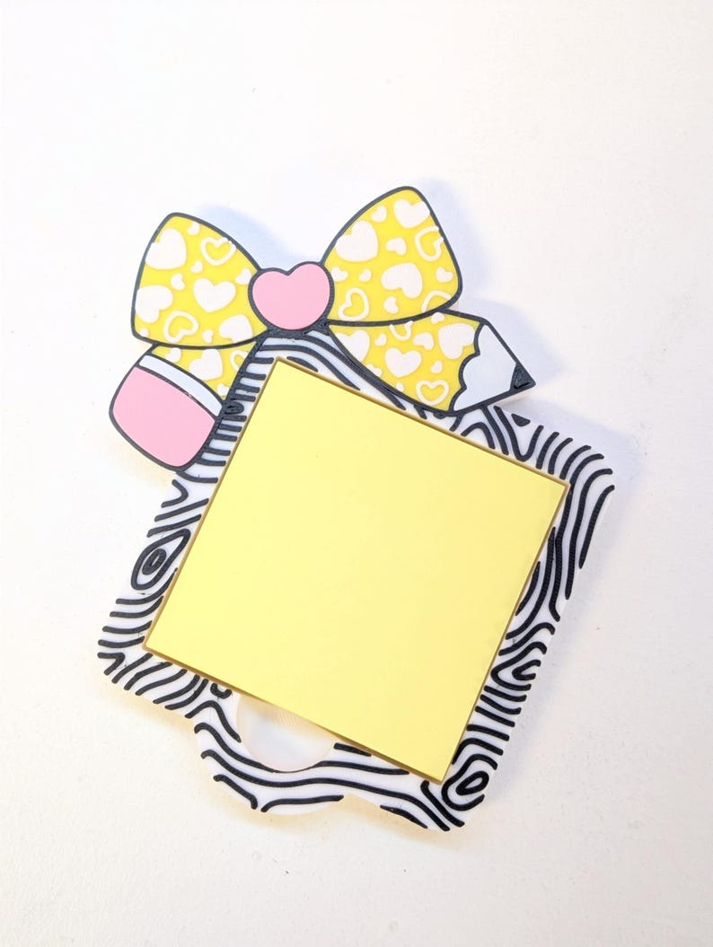 Peut inclure: Un porte-m&eacute;mo d&eacute;coratif avec un n&oelig;ud jaune &agrave; c&oelig;urs blancs, un c&oelig;ur rose et un crayon. Le porte-m&eacute;mo a un carr&eacute; jaune pour les notes, pos&eacute; sur un cadre &agrave; motifs noir et blanc. Un design mignon et fantaisiste.