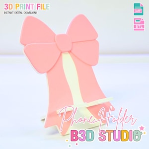 Puede incluir: Un soporte para teléfono en forma de lazo rosa con un centro color crema. Las palabras "Phone Holder" y "B3D STUDIO" están escritas en la parte delantera. La imagen también incluye el texto "3D PRINT FILE" y "INSTANT DIGITAL DOWNLOAD".
