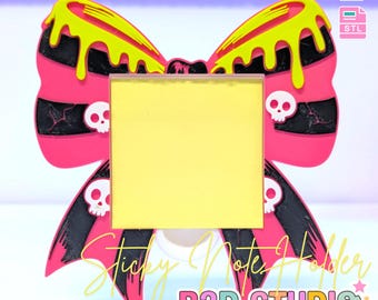 May include: A pink and black bow-shaped sticky note holder with yellow dripping accents and skull details. The holder has a yellow square for notes and the text "Sticky Note Holder" and "B3D STUDIO". The image also includes the text "3D PRINT FILE".