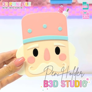 Puede incluir: Un original portalápices con forma de cascanueces, con un sombrero rosa, ribete azul y una cara color crema con ojos negros y bigote blanco. El texto "Pen Holder" y "B3D STUDIO" están en la imagen. La imagen también incluye el texto "3D PRINT FILE" y "INSTANT DIGITAL DOWNLOAD".
