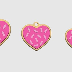 May include: Three heart-shaped charms with a pink frosted design and sprinkles. The charms have a gold-colored border and a small hole at the top for hanging. The sizes vary, with the largest charm on the left and the smallest on the right.