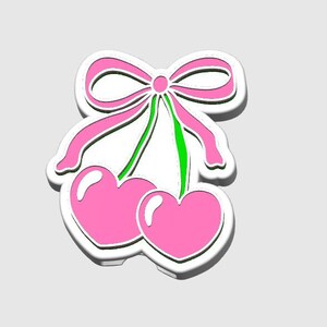 May include: A sticker featuring a pair of pink heart-shaped cherries with a pink bow and green stems. The design has a white outline and a subtle shadow, giving it a 3D effect. The background is a solid light gray.