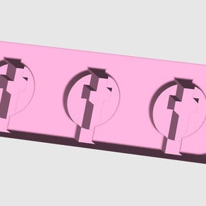 May include: A light pink, rectangular mold with three circular cavities. Each cavity has a stylized, geometric design. The mold is designed for creating multiple identical objects.