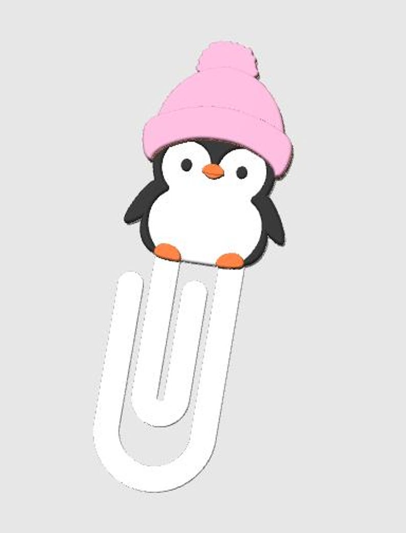 May include: A whimsical penguin-shaped bookmark. The penguin has a black body, white belly, orange feet and beak, and a pink knit cap with a pom-pom. The bookmark is white and has a unique, curved design.