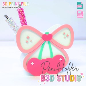 Könnte beinhalten: Ein rosa-weißer Stifthalter in Form einer Schleife und Kirschen, mit dem Text "Pen Holder" und "B3D STUDIO". Zwei dekorative Stifte befinden sich im Halter. Das Bild enthält auch den Text "3D PRINT FILE" und "INSTANT DIGITAL DOWNLOAD".