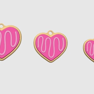 May include: Three heart-shaped charms in varying sizes. Each charm features a pink heart with a white icing design and a gold-colored border. A small hole is at the top of each charm.