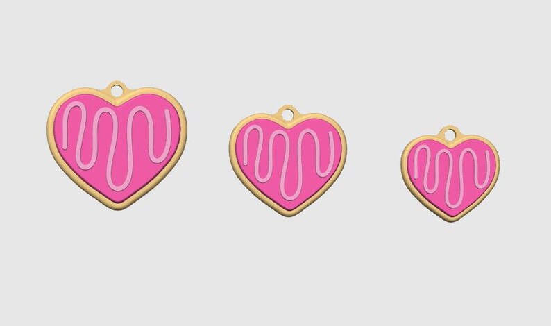 May include: Three heart-shaped charms in varying sizes. Each charm features a pink heart with a white icing design and a gold-colored border. A small hole is at the top of each charm.