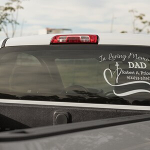 May include: A white pickup truck with a white vinyl decal on the rear window. The decal reads "In Loving Memory DAD Robert A. Price Jr. 9/21/53-5/19/21".