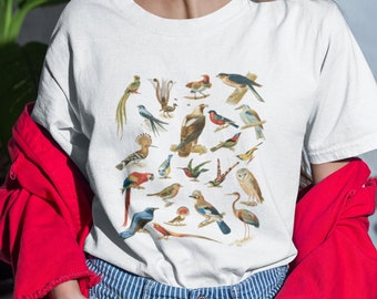 Puede incluir: Una camiseta blanca con una ilustración vintage colorida de varias aves. Las aves se representan en una variedad de poses y colores, incluyendo azul, rojo, verde y amarillo.