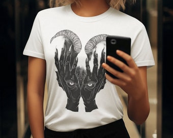 May include: A white short-sleeved t-shirt featuring a black and white graphic print of two hands with long, pointed fingers and curved horns, with a pair of eyes visible between the palms. The shirt is worn with black pants and a black smartphone.