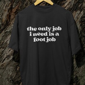Puede incluir: Camiseta negra con texto blanco que dice "the only job i need is a foot job".