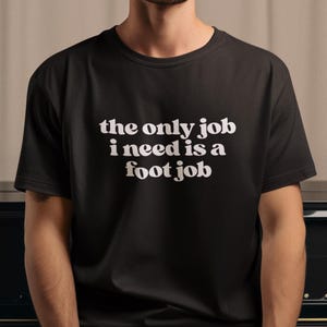 Puede incluir: Una camiseta negra con texto blanco que dice "the only job i need is a foot job".