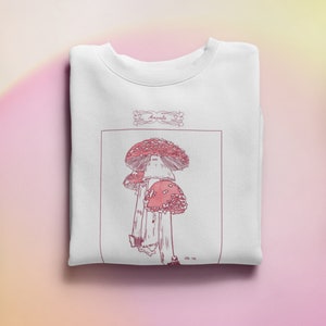 K&ouml;nnte beinhalten: Wei&szlig;es Sweatshirt mit einer Illustration von rosa und roten Pilzen und dem Text "Amanda" in einem dekorativen Rahmen.