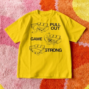 May include: A yellow t-shirt with a black graphic of a person pulling out a sofa bed drawer, with the words "PULL OUT GAME STRONG" and "GAME" printed on the shirt.
