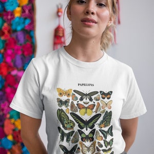 Może przedstawiać: Biały t-shirt z vintage'ową ilustracją motyli. Ilustracja jest w odcieniach brązu, zieleni, ż&oacute;łci i błękitu. Tekst "PAPILLONS" jest nadrukowany nad ilustracją.