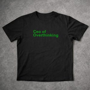 May include: A black short-sleeved t-shirt featuring the text "Ceo of Overthinking" printed in a bold, bright green sans-serif font across the centre of the chest. The garment has a standard crew neckline and a straight hemline design.