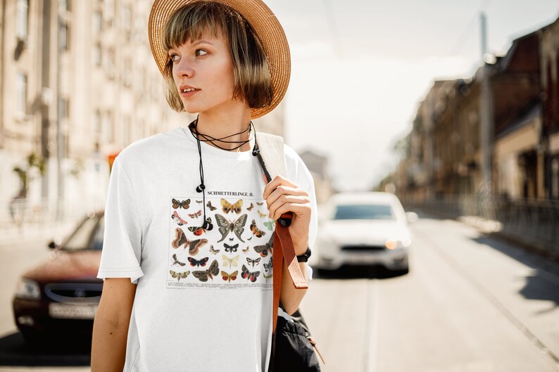 Puede incluir: Una camiseta blanca con una ilustraci&oacute;n vintage de mariposas impresa en la parte delantera. La ilustraci&oacute;n se titula "Schmetterlinge II".