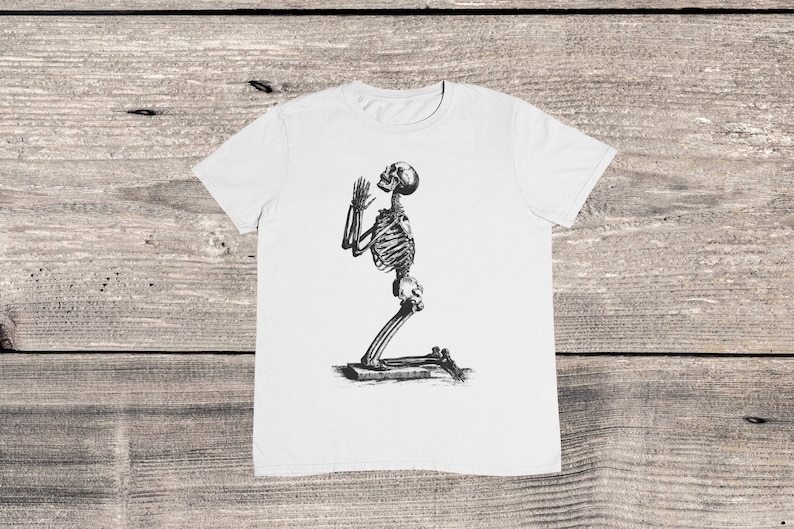 May include: White t-shirt with a black and white illustration of a skeleton kneeling and praying.