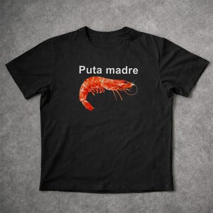May include: Black t-shirt featuring the phrase "Puta madre" above a vibrant red shrimp illustration. The design is centered on the shirt, offering a bold and eye-catching statement. The shirt is made of a soft material.