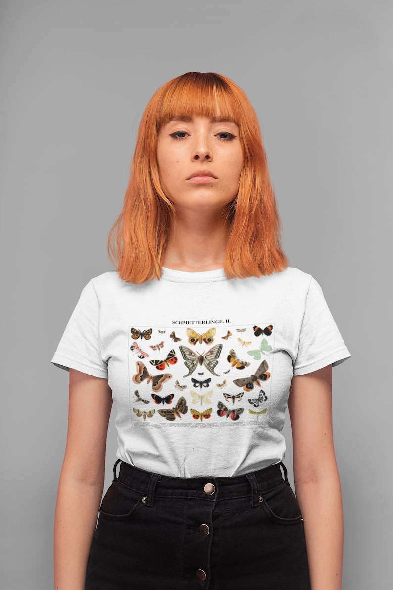 Puede incluir: Camiseta blanca con una ilustraci&oacute;n vintage de una colecci&oacute;n de mariposas. La ilustraci&oacute;n est&aacute; en tonos de marr&oacute;n, naranja, amarillo, blanco y negro. El texto "SCHMETTERLINGE II." est&aacute; impreso sobre la ilustraci&oacute;n.