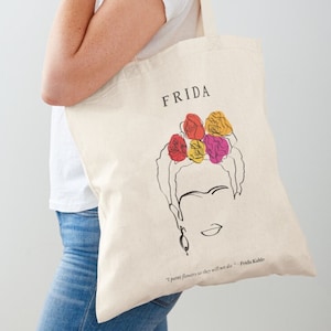 Könnte beinhalten: Eine weiße Canvas-Tragetasche mit einer schwarzen Linienzeichnung von Frida Kahlo mit Blumen im Haar. Der Spruch "Ich male Blumen, damit sie nicht sterben" - Frida Kahlo ist auf der Tasche aufgedruckt.