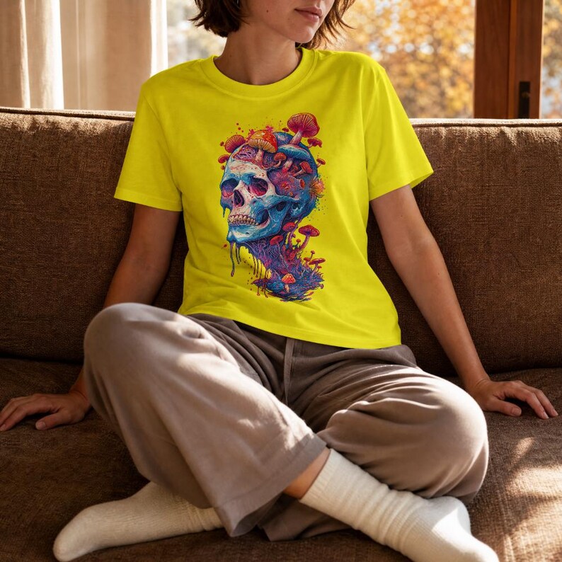 Op de afbeelding: Een felgeel T-shirt met korte mouwen en een grafische print van een blauwe en paarse schedel, met diverse rode en oranje paddenstoelen die uit de bovenkant en de basis groeien. Het schedelontwerp heeft een druipend effect en details.