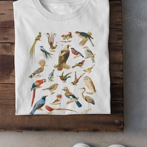 May include: White t-shirt with a colorful illustration of various birds. The birds are depicted in a vintage style and are arranged in a circular pattern.