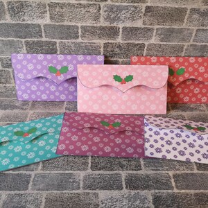 May include: Five different patterned paper envelopes with a holly design. The envelopes are in shades of purple, pink, red, teal, and burgundy.