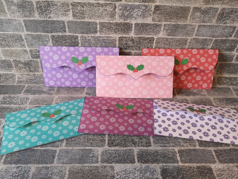 May include: Five different patterned paper envelopes with a holly design. The envelopes are in shades of purple, pink, red, teal, and burgundy.