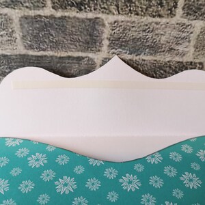 May include: A white card with a scalloped edge and a strip of adhesive tape. The card has a teal background with a white snowflake pattern.