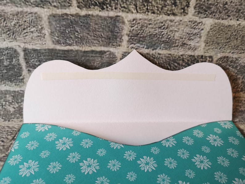 May include: A white card with a scalloped edge and a strip of adhesive tape. The card has a teal background with a white snowflake pattern.