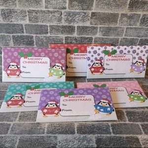 May include: Set of six purple, pink, blue, and green gift tags with a penguin wearing a red, green, or purple sweater. Each tag has a snowflake and flower pattern and says "Merry Christmas" with a space for "To:" and "From:".