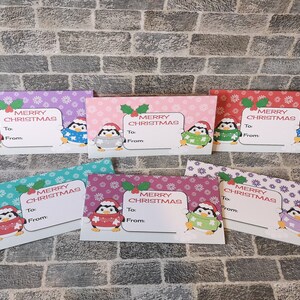May include: Six colorful gift tags featuring a penguin wearing a sweater and a Santa hat. Each tag has a snowflake pattern and says "Merry Christmas" with space to write "To" and "From".